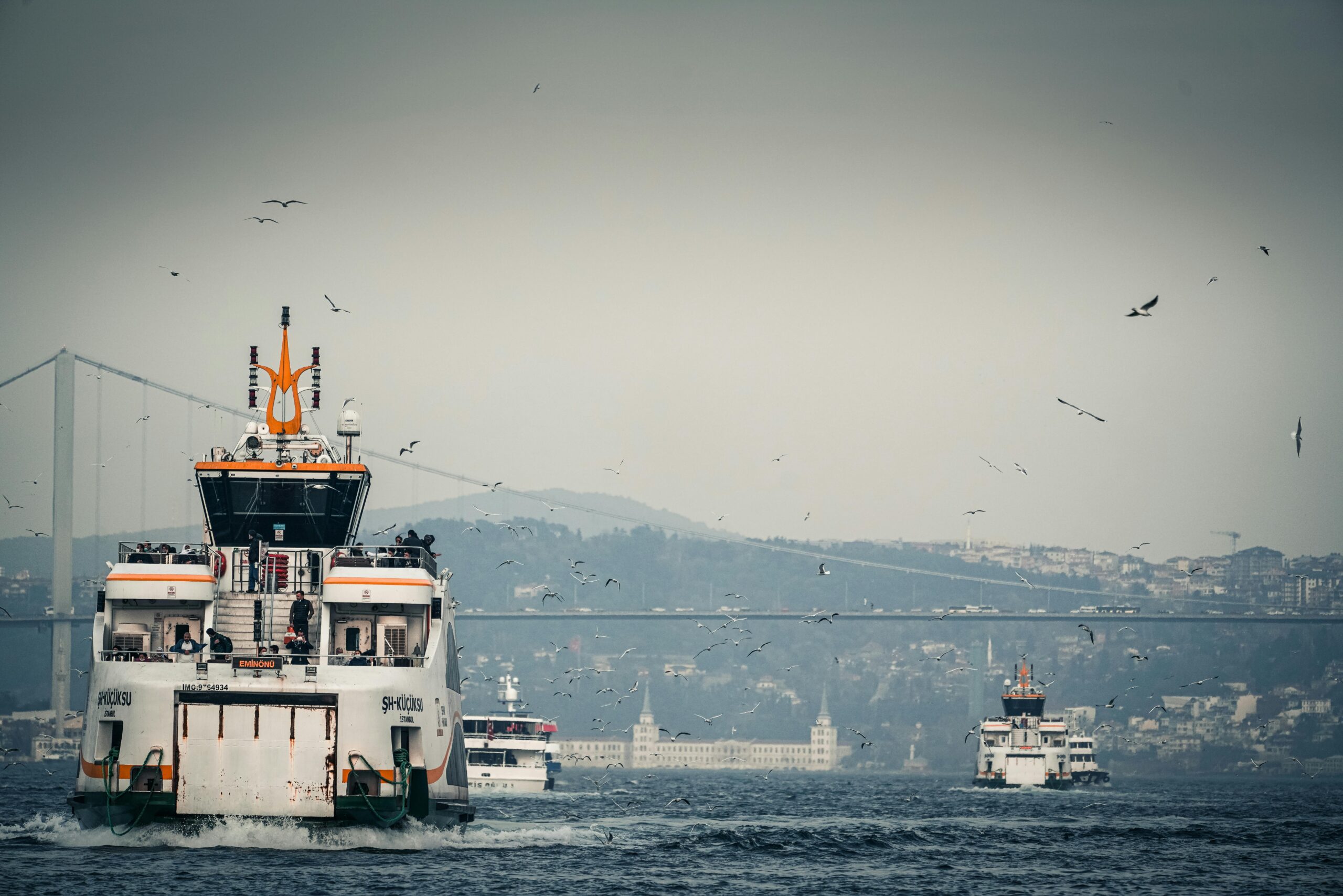 Ferries navigating the Bosphorus in Istanbul with cityscape and bridge in the background.